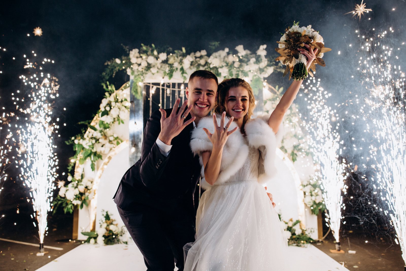 Newlyweds on the background of the wedding arch. Night fireworks.